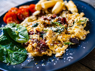 Breakfast - scrambled eggs with vegetables and grissini on wooden background