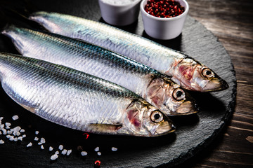 Fresh raw herrings served on black stone on wooden table