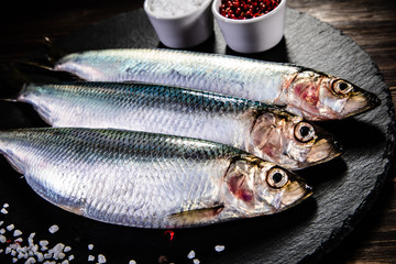 Fresh raw herrings served on black stone on wooden table