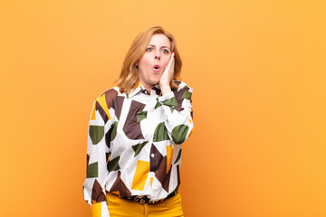 middle age woman feeling shocked and astonished holding face to hand in disbelief with mouth wide...