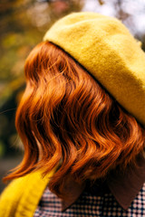 A beautiful red-haired woman with a curly hairstyle walking in the park. Fashionable autumn clothes...