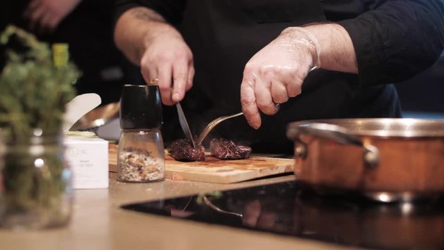 Juicy freshly baked meat on a wooden cutting board. Chef's hands cut off a piece of steak with a knife and fork on the kitchen. Man cuts off a piece of beef steak on the kitchen of restaurant. 