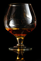 Glass of cognac on black reflective glass