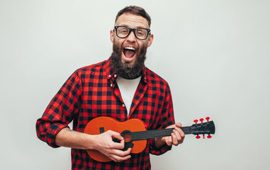 Handsome hipster guy plays ukulele guitar isolate over white background