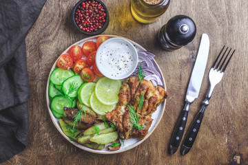 Lunch bowl with grilled chicken, red onion, tomato, cucumber, lemon, olive and sause on wooden background. Top view.