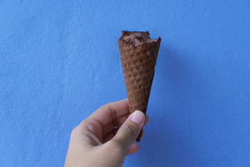 woman hand holding chocolate ice cream cone for summer refreshment on colorful blue background