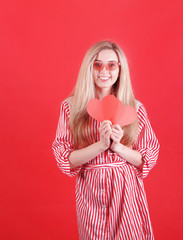 Smiling woman in red dress with paper heart  in hand posing on red background. Valentine`s Day concept.