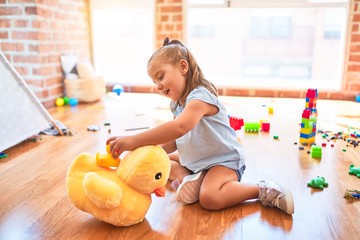 Young beautiful blonde girl kid enjoying play school with toys at kindergarten, smiling happy playing with stuffed animal at home