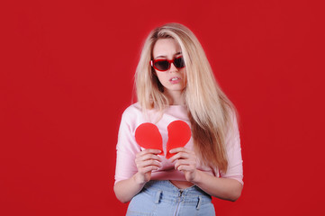 Young caucasian woman in sunglasses with broken red heart in hands. Valentine`s Day. Broken heart concept.