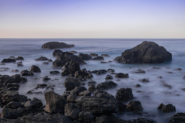Fototapeta na wymiar Volcanic rocks in Atlantic ocean, long exposure photography, horizon with sunset light, San Juan de la Rambla coastline, Tenerife, Canary islands, Spain