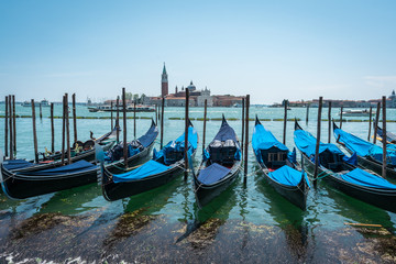 Fototapeta na wymiar Gondolas on the Grand Canal pier in Venice. San Giorgio Maggiore Island background. The row of beautiful bright colored Venetian gondolas mooring on berth. Jetty. Panoramic view of Venice lagoon.