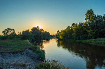 Sunset over the meandering river, which is hidden behind the crown of trees growing on the banks. Photos from the shore. Scenery of Teteriv river, which flows through Ukraine in Europe