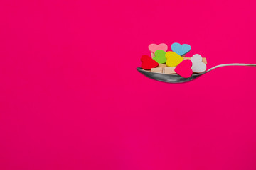 Composition for Valentine's Day. Colored hearts on clothespins in a spoon on a red background. Flat lay, copy space.