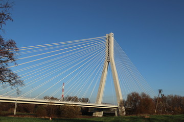 Fototapeta na wymiar Rzeszow, Poland - 9 9 2018: Suspended road bridge across the Wislok River. Metal construction technological structure. Modern architecture. A white cross on a blue background is a symbol of the city
