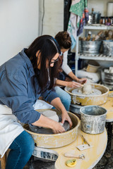 two ceramic artists working side by side at pottery wheels in an art studio trimming clay pots on pottery wheels