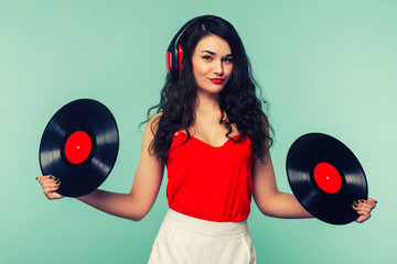 Young woman in headphones looking at camera and closing her face with vinyl record