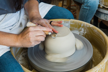 a caucasian woman trimming the base of an unfinished clay pot on a pottery wheel close up and adding detail work to the bottom
