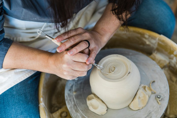 a caucasian woman trimming the base of an unfinished clay pot on a pottery wheel close up and...
