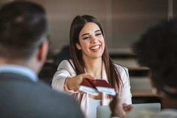 Beautiful female travel agent is working with clients in office and offering them tours. Young woman smiling and giving tickets, passport with visa to tourists. Close-up
