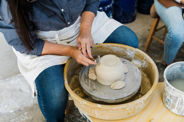 ceramic artist working at a pottery wheel in an art studio trimming clay pots