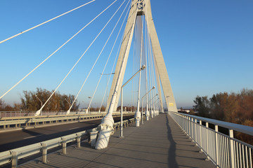 Fototapeta na wymiar Rzeszow, Poland - 9 9 2018: Suspended road bridge across the Wislok River. Metal construction technological structure. Modern architecture. A white cross on a blue background is a symbol of the city