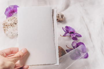 Wedding invitation mockup with orchid, papers on white textile background. Top view, flat lay. Wedding stationary. Perfect for presentation of your invitation, menu, greeting cards