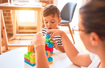 Obraz na płótnie Canvas Beautiful teacher and toddler boy playing with construction blocks bulding tower at kindergarten