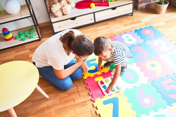 Beautiful teacher and toddler boy sitting on puzzle playing with numbers at kindergarten