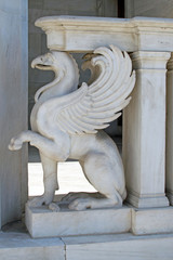 Griffin is a decoration element of an ancient building in Greece. White marble griffin. Mythical characters in architecture.