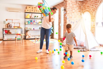Beautiful teacher and toddler boy playing with colored small balls at kindergarten