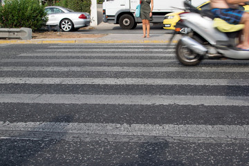 Pedestrian crossing on an asphalt road. A large stream of cars on the road. The girl is waiting for the opportunity to cross the road on a zebra.