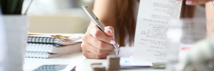 Focus on smart businesswoman sitting indoors and counting presumable profits from charts in important paper tablet with numbers. Lady making notes. Office concept. Blurred background
