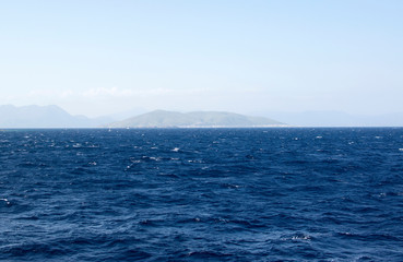 Obraz premium Dark blue sea against a background of blue sky and barely visible mountains on the horizon. Sea with small waves.