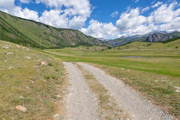 Fototapeta na wymiar Beautiful dirt road in the mountains of Altai, against the backdrop of mountains and clouds.
