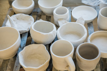 A shelf full of unfinished clay ceramic pottery pieces that are waiting to be fired in a kiln