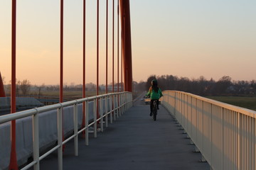Rzeszow, Poland - 9 9 2018: Suspended road bridge across the autobahn. Metal construction technological structure. Modern architecture. The girl rides a bike in the evening over the bridge