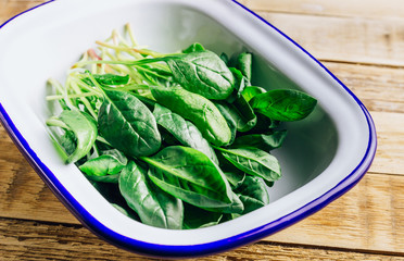 Fresh green baby spinach on plate on wooden rustic table. Healthy diet, vegetarian food concept.