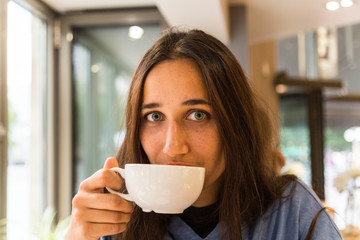 Young Woman with Coffee Mug on Lips Looking at Camera