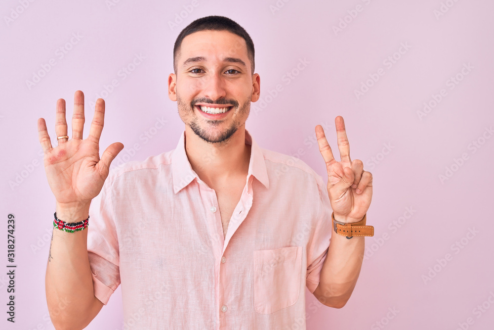 Wall mural Young handsome man wearing pink shirt standing over isolated background showing and pointing up with fingers number seven while smiling confident and happy.