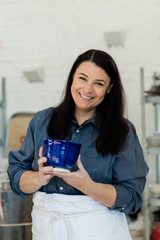 Creative Pottery Cermanic artist holding a blue piece of finished and glazed clay pottery in an art loft studio