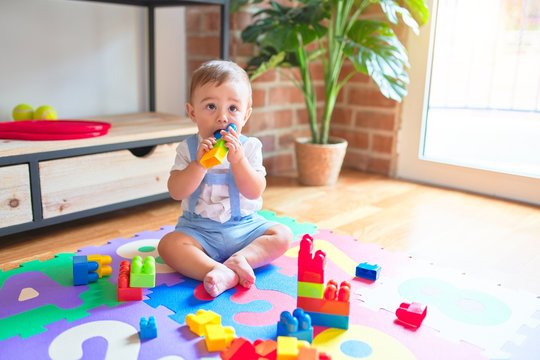Beautiful toddler sitting on puzzle carpet playing with building blocks at kindergarten