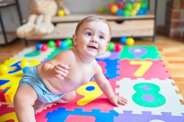 Beautiful toddler sitting on the puzzle carpet toy smiling at kindergarten