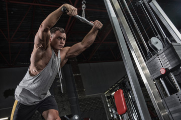Muscular athletic bodybuilder man hard workout in gym over dark background with dramatic light with...