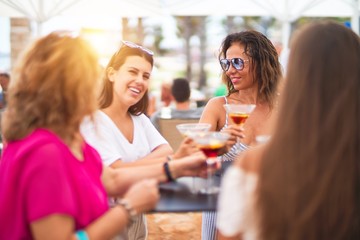 Beautiful group of women sitting at terrace of restaurant drinking cocktails speaking and smiling