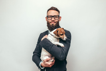 Handsome man with beard in formal suit hugs his cute dog Jack Russell Terrier isolate over white...