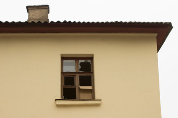 yellow, old, abandoned house with a broken window and a chimney