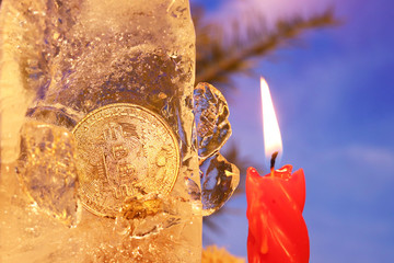 New Year's decoration. Bitcoin sunk into the ice and brightened by the flame of a red candle...