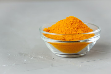 Ground turmeric in a glass plate on a gray background