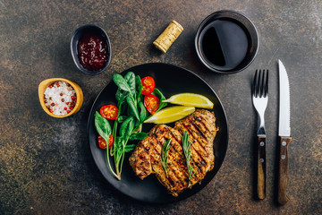 Roasted pork steak on black plate over dark background. With lemon, Cranberry Sauce and wine.