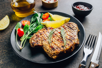Roasted pork steak on black plate over dark background. With lemon, Cranberry Sauce and wine.